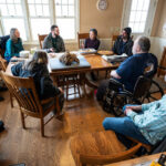 Photo of Farmers Jan Shepel (at near left) and Jim Koch (in wheelchair) flanking a 110-pound iron meteorite sitting on their family dining table at their home and Vienna EqHo Farm in the Town of Vienna, Wis. Included in the background, from left to right, are Shepel’s sister, Laurie Shepel; Carrie Eaton, curator of the UW Geology Museum; science writer Will Cushman; Noriko Kita, a distinguished scientist and meteorite expert from UW–Madison; and UW Geology Museum Director Rich Slaughter. At near right is Joe Zanter, a metallurgical engineer and Laurie Shepel’s husband. Photo: Jeff Miller