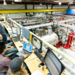 Photo of Elliot Claveau, honorary fellow in the Department of Physics and experimental scientist at Realta Fusion, raising his hands in celebration of achieving a plasma from the control room at the Wisconsin HTS Axisymmetric Mirror Project (WHAM) experiment being conducted at the Wisconsin Plasma Physics Laboratory in Stoughton on July 16, 2024. Photo: Bryce Richter