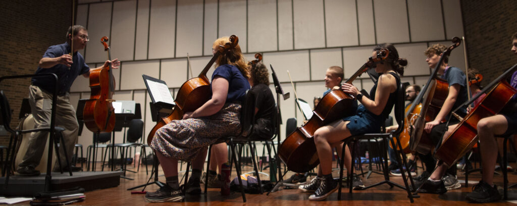 Photo of Professor Benjamin Whitcomb, left, taking an athlete’s stance as he coaches camp musicians. Strings Camp students work to refine their music for a performance in Young Auditorium on the UW-Whitewater campus. (UW-Whitewater photo/Craig Schreiner)