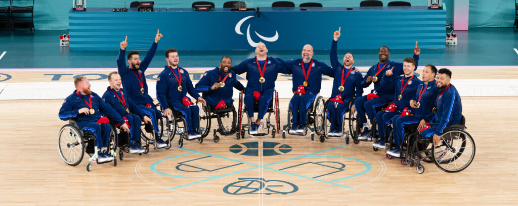 Photo of members of the USA men’s wheelchair basketball team shown shortly after receiving their gold medals at the Paris 2024 Paralympic Games. From left, Jeromie Meyer, John Boie, Fabian Romo, AJ Fitzpatrick, Trevon Jenifer, Nate Hinze, Paul Schulte, Steve Serio, Brian Bell, Talen Jourdan, Jake Williams, and Jorge Salazar. Meyer, Boie, Fitzpatrick, Hinze, Jourdan, and Williams are all Warhawks, either current or former members of the UW-Whitewater men’s wheelchair basketball team. (Photo courtesy of the USOPC)