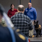 Photo of Lani Rethaber, executive director of Patriot K9s of Wisconsin, standing next to his German Shepherd Aisa as UW-River Falls student Michaela Hasapopoulos, left, sings the national anthem at the beginning of a Veterans Day ceremony at the university.